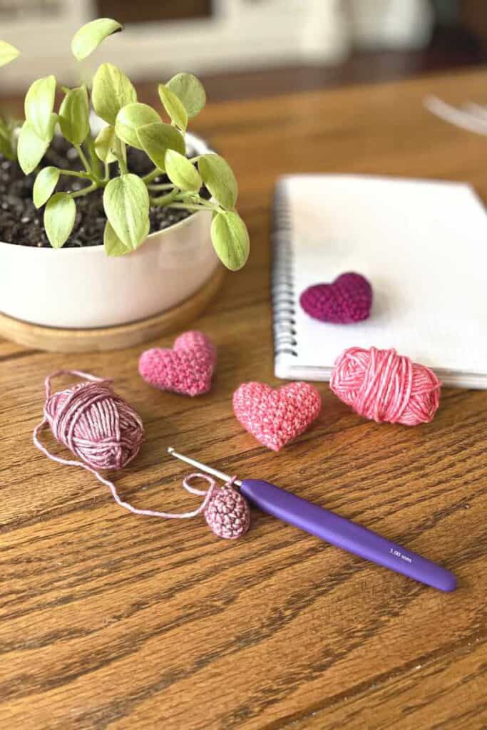 Amigurumi hearts, with small balls of yarn, near plants and notebook